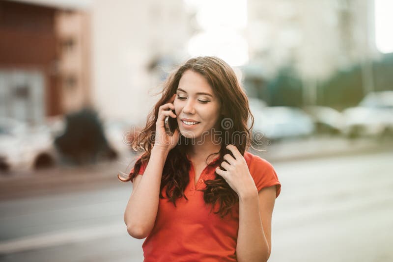 La jolie fille dans le tenue décontractée parle à un téléphone portable tout en marchant à la rue de ville un temps de coucher du photos libres de droits La jolie fille dans le tenue décontractée parle à un téléphone portable tout en marchant à la rue de ville un temps de coucher du photos libres de droits