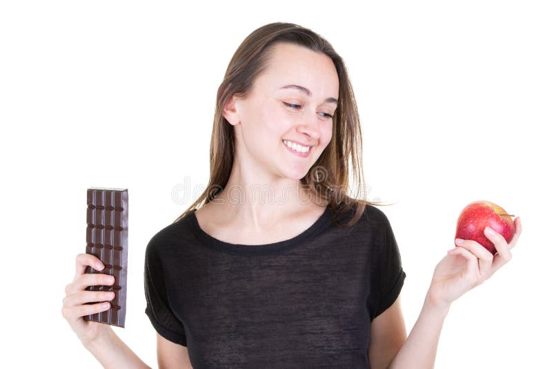 La jolie jeune femme avec la barre rouge de pomme et de chocolat tentée essayent d'être en bonne santé images libres de droits La jolie jeune femme avec la barre rouge de pomme et de chocolat tentée essayent d'être en bonne santé images libres de droits