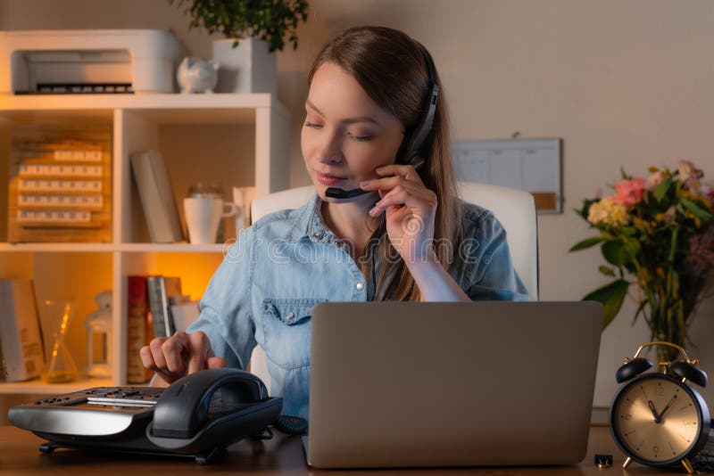 The young beautiful girl in jeans shirt working at her home office with headset and use laptop and fax. Operator call center. Freelance,. The young beautiful girl in jeans shirt working at her home office with headset and use laptop and fax. Operator call center. Freelance,