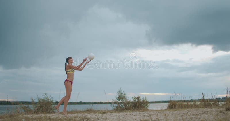 La jugadora de voleibol está sirviendo una pelota en una cancha de arena, toma completa de una mujer deportista en salto
