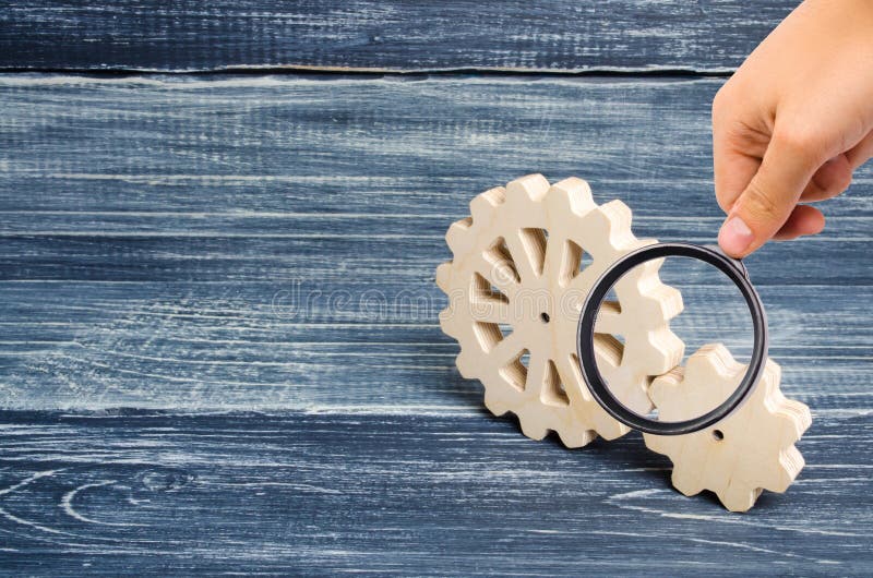 La lente d'ingrandimento sta esaminando gli ingranaggi del supporto di legno su un fondo di legno scuro Concetto di tecnologia e fotografie stock La lente d'ingrandimento sta esaminando gli ingranaggi del supporto di legno su un fondo di legno scuro Concetto di tecnologia e fotografie stock