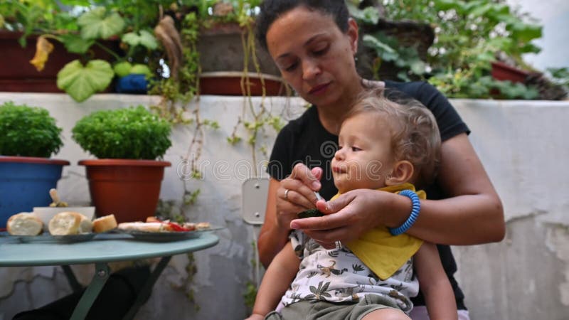 La madre alimenta a su hijo pequeño con amor y comida saludable en un tranquilo jardín que hace hincapié en el cuidado y la unión almacen de metraje de vídeo