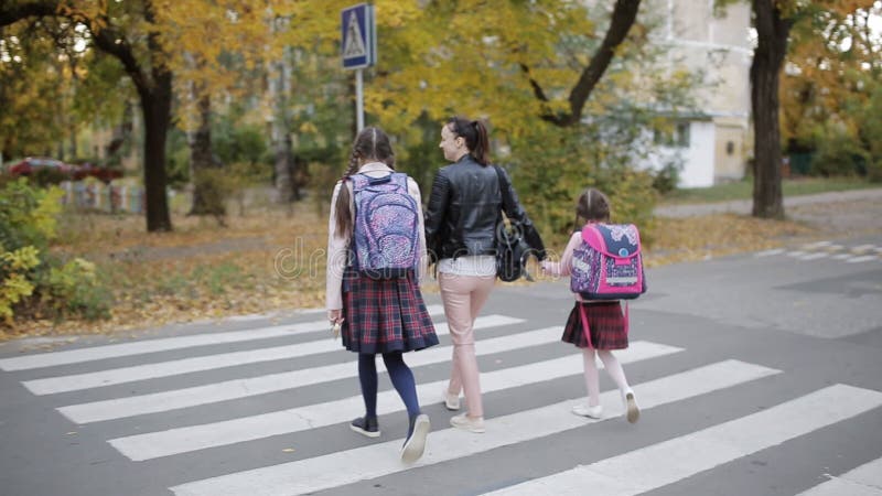 La madre con le sue figlie nella caduta va a casa dopo scuola ed attraversa la strada ad un attraversamento archivi video