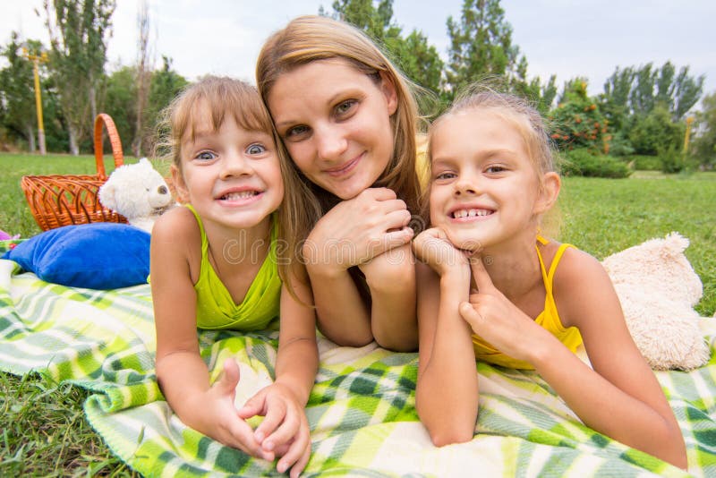 La madre e due ragazze che si trovano sull'erba su un picnic e su un divertimento esaminano la struttura immagini stock libere da diritti La madre e due ragazze che si trovano sull'erba su un picnic e su un divertimento esaminano la struttura immagini stock libere da diritti