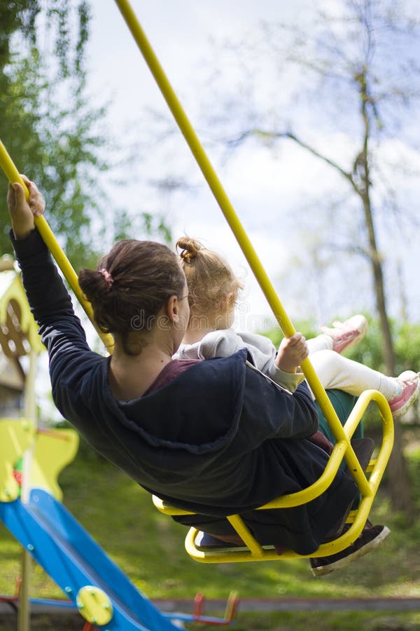 La madre e la figlia si divertono nel parco dei bambini su un'oscillazione fotografia stock La madre e la figlia si divertono nel parco dei bambini su un'oscillazione fotografia stock