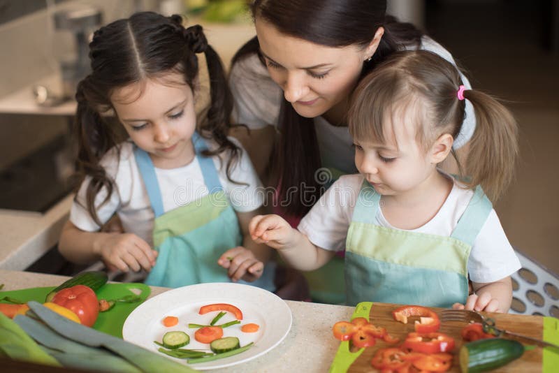 La madre ed i bambini felici della famiglia stanno preparando l'alimento sano, essi improvvisano insieme nella cucina immagini stock La madre ed i bambini felici della famiglia stanno preparando l'alimento sano, essi improvvisano insieme nella cucina immagini stock