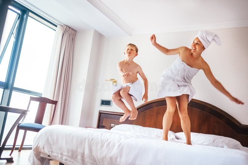 La madre ed il figlio saltano sul letto nella stanza di albergo di lusso immagini stock libere da diritti La madre ed il figlio saltano sul letto nella stanza di albergo di lusso immagini stock libere da diritti