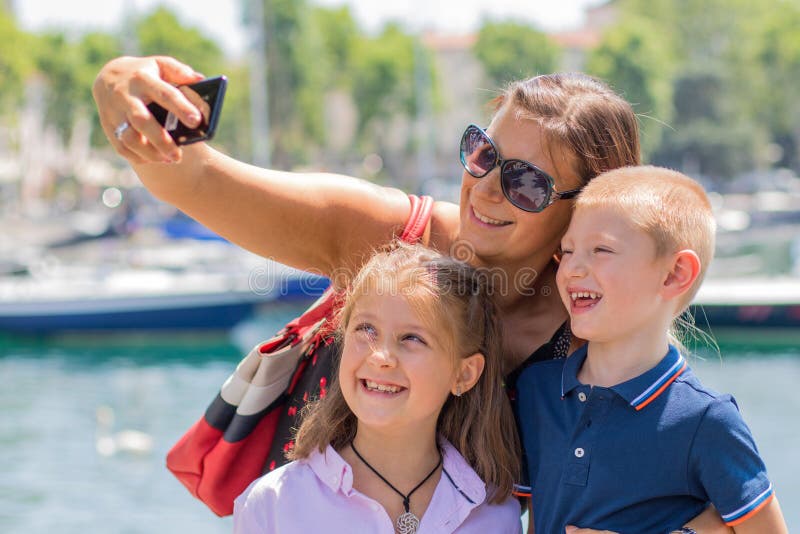 La madre feliz con sus niños está tomando un selfie en un día soleado foto de archivo La madre feliz con sus niños está tomando un selfie en un día soleado foto de archivo