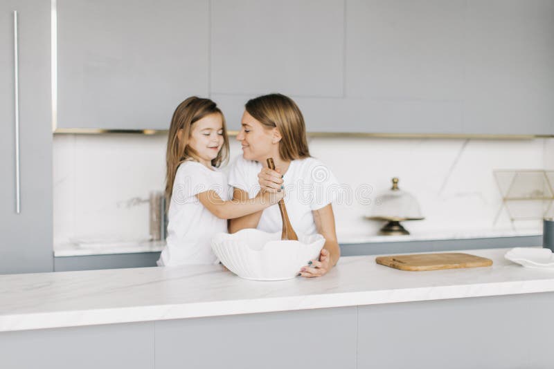 La madre hermosa joven con su pequeña hija está cocinando imagen de archivo libre de regalías La madre hermosa joven con su pequeña hija está cocinando imagen de archivo libre de regalías