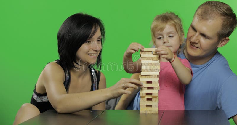 La madre, il padre e la figlia gioca il jenga Tira i blocchi di legno dalla torre immagini stock La madre, il padre e la figlia gioca il jenga Tira i blocchi di legno dalla torre immagini stock