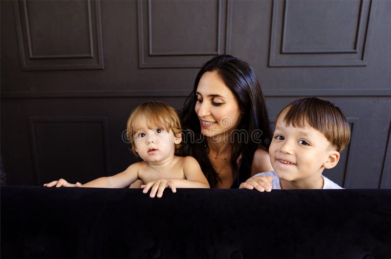 La madre joven y sus dos niños pequeños juegan en casa. Mujer con ropa informal se está divirtiendo con sus lindos hijos en la sal fotos de archivo