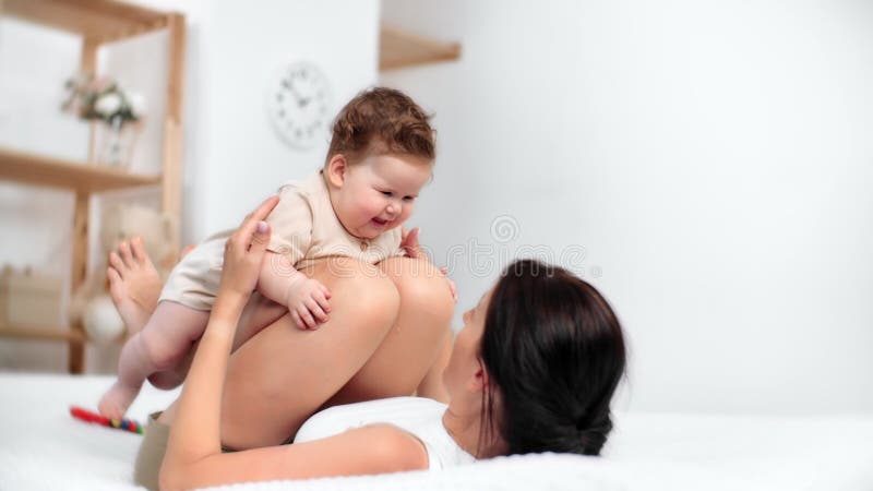 La madre se reclina con cuidado sobre la cama blanca cuna recién nacido en regazo compartiendo momentos íntimos de unión con caric metrajes