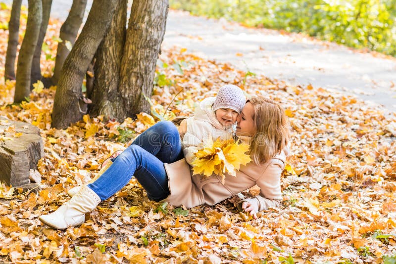 La madre y el bebé felices de la familia ríen con las hojas en otoño de la naturaleza