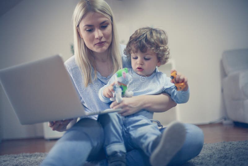 La madre y el hijo tienen juego junto, mamá que usa el ordenador portátil fotografía de archivo libre de regalías La madre y el hijo tienen juego junto, mamá que usa el ordenador portátil fotografía de archivo libre de regalías