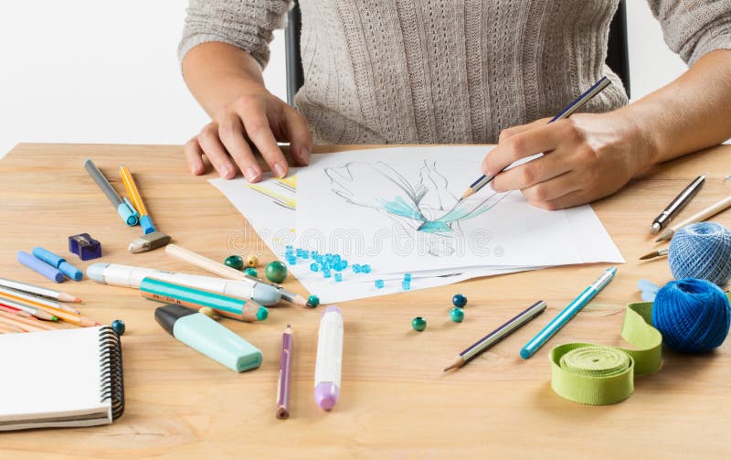 La main avec une brosse dessine un croquis à la mode sur un fond de livre blanc parmi des brosses et des peintures images libres de droits