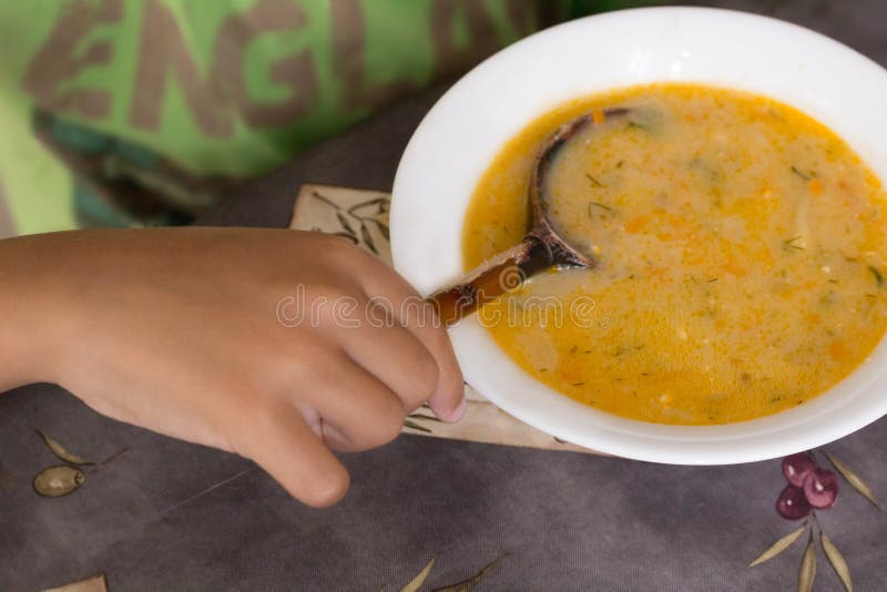 La main d'enfant tient une cuillère mangeant de la soupe à fromage photographie stock La main d'enfant tient une cuillère mangeant de la soupe à fromage photographie stock