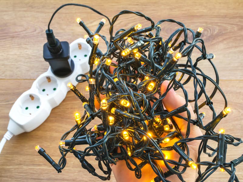 La main d'une femme tient les lumières de Noël brillantes Prise d'alimentation noire de la guirlande électrique insérée dans une photo libre de droits La main d'une femme tient les lumières de Noël brillantes Prise d'alimentation noire de la guirlande électrique insérée dans une photo libre de droits