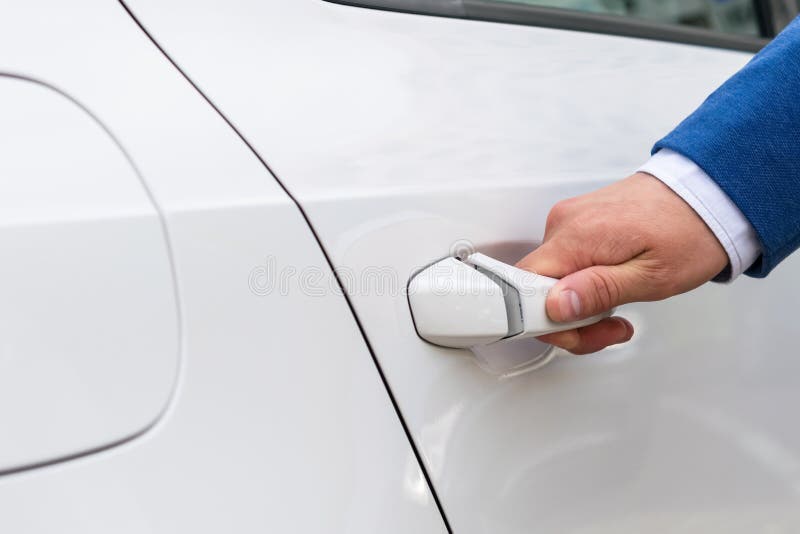 La main dans le costume bleu ouvre la portière de voiture blanche, plan rapproché photographie stock La main dans le costume bleu ouvre la portière de voiture blanche, plan rapproché photographie stock