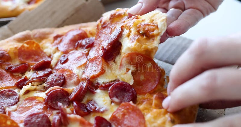 La main de la femme déchire un morceau de pizza chaude