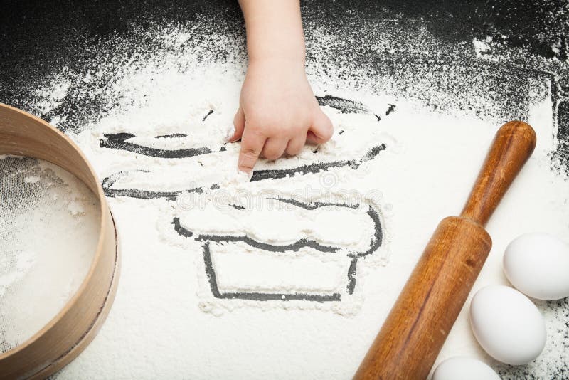 La main de l'enfant joue avec de la farine sur la table de cuisine images libres de droits La main de l'enfant joue avec de la farine sur la table de cuisine images libres de droits