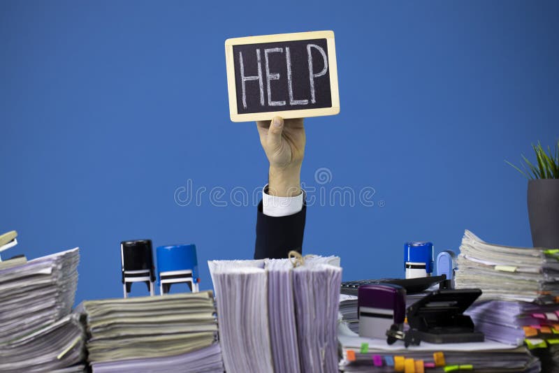 Hand of caucasian businessman emerging from office desk loaded of paperwork, invoices and lot of papers and documents. Hand of caucasian businessman emerging from office desk loaded of paperwork, invoices and lot of papers and documents