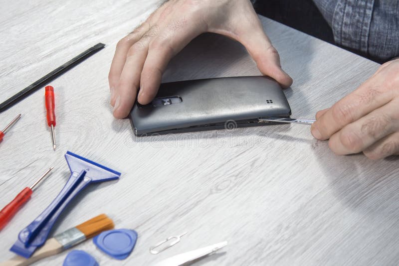 La main de l'homme enlève la couverture du téléphone portable utilisant l'outil photographie stock libre de droits La main de l'homme enlève la couverture du téléphone portable utilisant l'outil photographie stock libre de droits