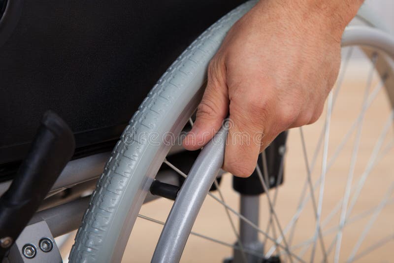 La main de l'homme handicapé poussant la roue du fauteuil roulant photographie stock La main de l'homme handicapé poussant la roue du fauteuil roulant photographie stock