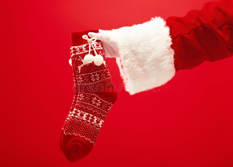La main de Santa Claus tenant Noël a tricoté des chaussettes sur le fond rouge photographie stock libre de droits La main de Santa Claus tenant Noël a tricoté des chaussettes sur le fond rouge photographie stock libre de droits