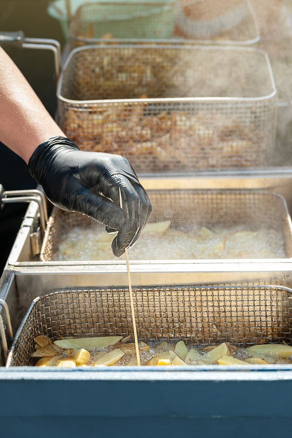 La main du chef v?rifie la qualit? des pommes de terre frites Pommes frites frites en huile de ?bullition dans une friteuse photographie stock La main du chef v?rifie la qualit? des pommes de terre frites Pommes frites frites en huile de ?bullition dans une friteuse photographie stock