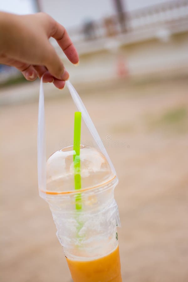 La main du ` s de femme tient une tasse en plastique de thé thaïlandais, photo à l'arrière-plan brouillé photo libre de droits La main du ` s de femme tient une tasse en plastique de thé thaïlandais, photo à l'arrière-plan brouillé photo libre de droits