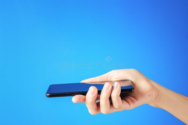 La main femelle tient le smartphone noir sur le fond bleu images stock La main femelle tient le smartphone noir sur le fond bleu images stock