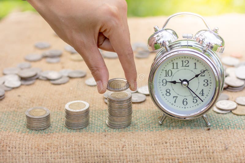 La main humaine met la pièce de monnaie à la pile croissante de pièce de monnaie avec l'horloge, Sav image libre de droits La main humaine met la pièce de monnaie à la pile croissante de pièce de monnaie avec l'horloge, Sav image libre de droits