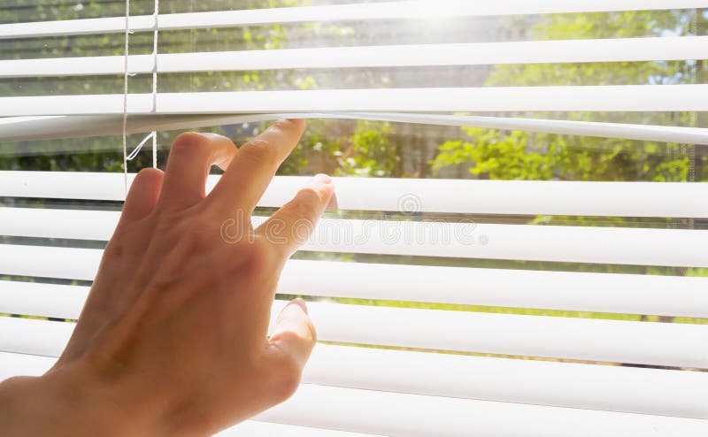 La main s'ouvre avec des aveugles de doigts, en dehors de fenêtre il y a lumière du soleil et arbres verts Été chaud de concept e photographie stock libre de droits La main s'ouvre avec des aveugles de doigts, en dehors de fenêtre il y a lumière du soleil et arbres verts Été chaud de concept e photographie stock libre de droits