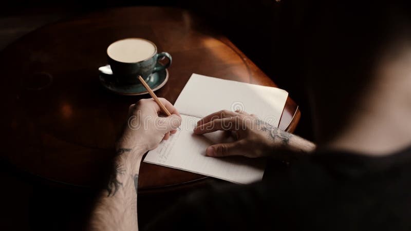 La main tatou? e de l'homme? crit dans un carnet sur une table basse dans un plan rapproch? de caf? banque de vidéos