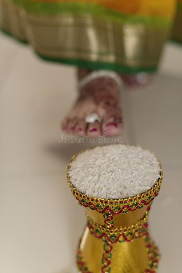 La maison du marié entrant de jeune mariée indoue indienne après l'avoir épousé en poussant le pot a rempli du riz avec son pied. image libre de droits La maison du marié entrant de jeune mariée indoue indienne après l'avoir épousé en poussant le pot a rempli du riz avec son pied. image libre de droits