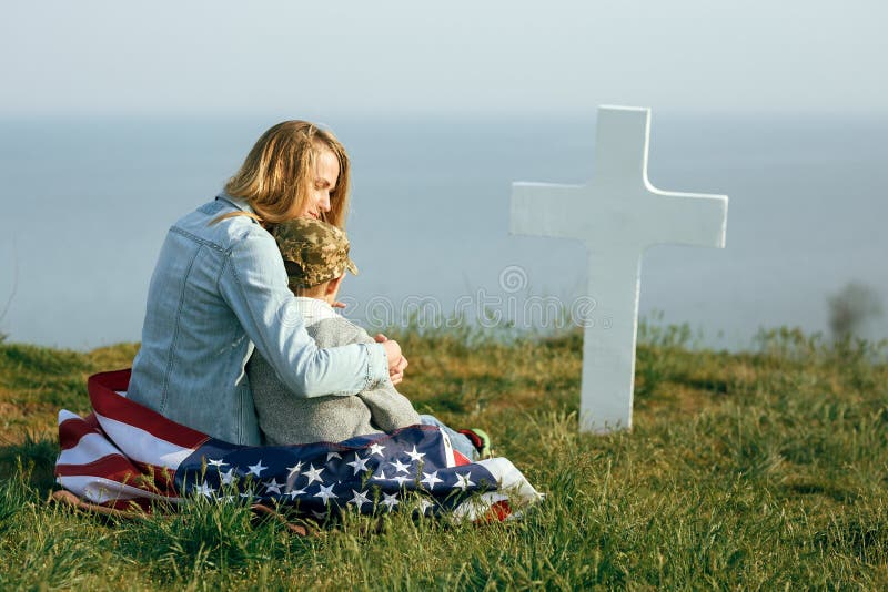 La mam? y el hijo se est?n sentando en el sepulcro de un soldado La mam? trajo a su hijo al sepulcro de su padre el Memorial Day fotos de archivo libres de regalías La mam? y el hijo se est?n sentando en el sepulcro de un soldado La mam? trajo a su hijo al sepulcro de su padre el Memorial Day fotos de archivo libres de regalías