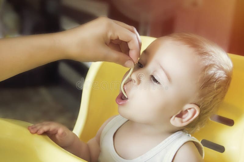 La maman alimente les petites nouilles de bébé garçon dans le highchair images libres de droits La maman alimente les petites nouilles de bébé garçon dans le highchair images libres de droits