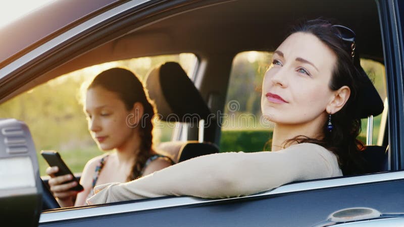 La maman et la fille 11 années se reposent dans la voiture dans un endroit pittoresque au coucher du soleil Une femme regarde la