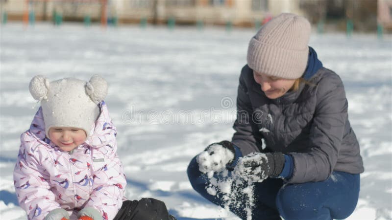 La mamma e la figlia si divertono sulla via in un giorno nevoso del bello inverno, la mia neve dei tiri della madre alla ragazza