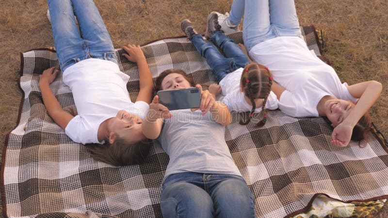 La mamma e i bambini felici fotografati sul palmare in parco. La madre e le figlie assumono un selfie mentre mentire di viaggio stock footage