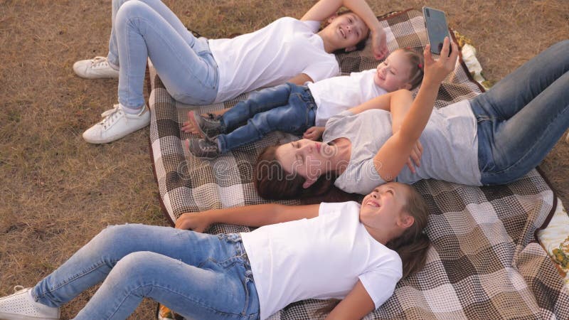 La mamma e i bambini felici fotografati sul palmare in parco. La madre e le figlie assumono un selfie mentre mentire di viaggio archivi video