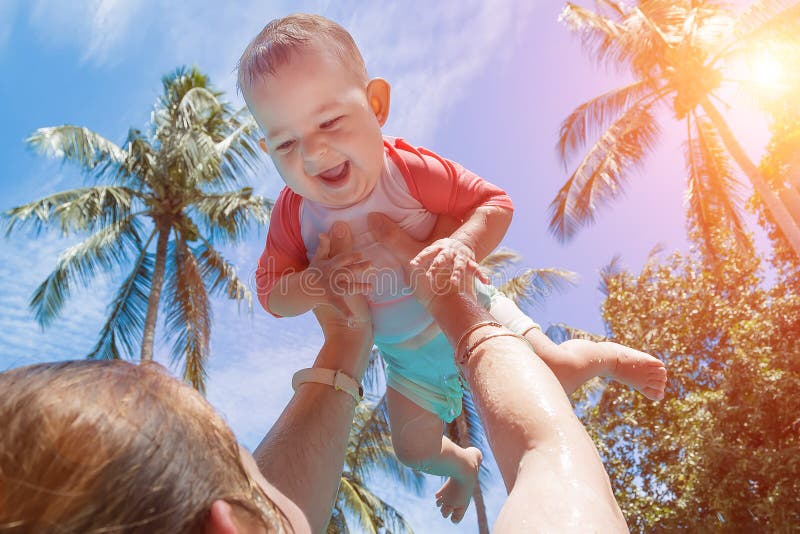La mamma ha alzato il bambino sopra la sua testa Bambino molto felice e di risata in un vestito di nuoto nelle armi della mamma V immagini stock libere da diritti La mamma ha alzato il bambino sopra la sua testa Bambino molto felice e di risata in un vestito di nuoto nelle armi della mamma V immagini stock libere da diritti