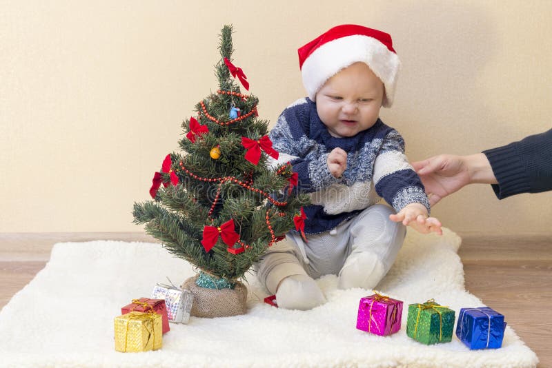 La mamá lleva a cabo la mano de un niño contrariedad en un sombrero de Papá Noel