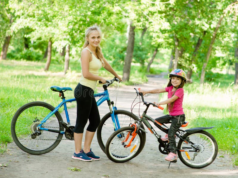 La mamá y la hija montan las bicis en el parque imagenes de archivo La mamá y la hija montan las bicis en el parque imagenes de archivo