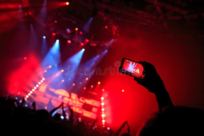 La mano con un smartphone registra el festival de música en directo, tomando la foto de la etapa del concierto fotografía de archivo libre de regalías La mano con un smartphone registra el festival de música en directo, tomando la foto de la etapa del concierto fotografía de archivo libre de regalías