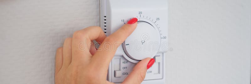 La mano de la mujer ajusta o activa el botón controlador de temperatura de la pared fotografía de archivo libre de regalías