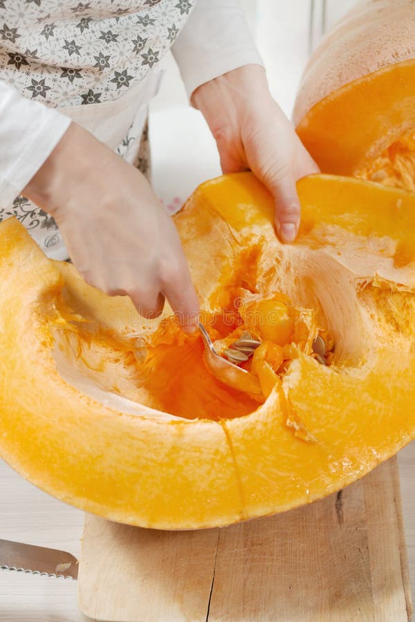 La mano de la mujer elige la pulpa desde el centro de una gran calabaza fresca con semillas Una mujer con un delantal de cocina U imagenes de archivo La mano de la mujer elige la pulpa desde el centro de una gran calabaza fresca con semillas Una mujer con un delantal de cocina U imagenes de archivo