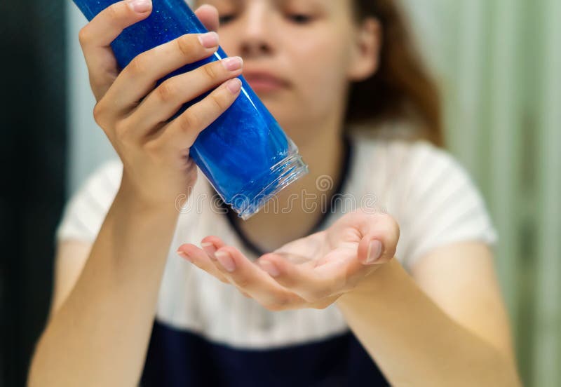 La mano de una adolescente vierte el lima azul de una botella transparente a la palma de la mano. un frasco de plástico con una ti fotografía de archivo libre de regalías