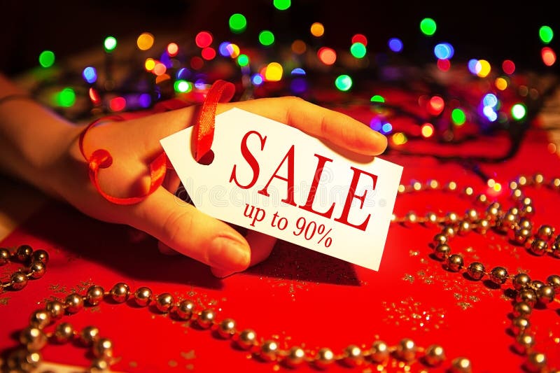 A woman`s hand holds a label with the text - a sale, with a 90 discount, on a decorated Christmas background, during the Christmas and New Year holidays. A woman`s hand holds a label with the text - a sale, with a 90 discount, on a decorated Christmas background, during the Christmas and New Year holidays.