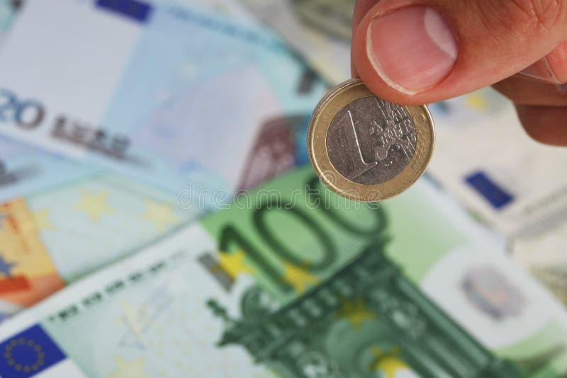 La mano del hombre que sostiene una moneda euro en billetes de banco euro imagenes de archivo La mano del hombre que sostiene una moneda euro en billetes de banco euro imagenes de archivo